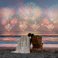 Quilt with star and stripe pattern in pastel colors on a white background. The quilt is draped on the back of a chair as a couple watches fireworks in the distance.