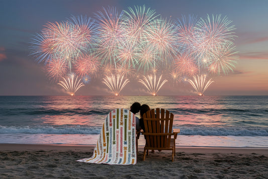 Quilt with star and stripe pattern in pastel colors on a white background. The quilt is draped on the back of a chair as a couple watches fireworks in the distance.