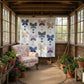 Sunroom with butterfly-patterned quilt on wall, armchair, and potted plants.