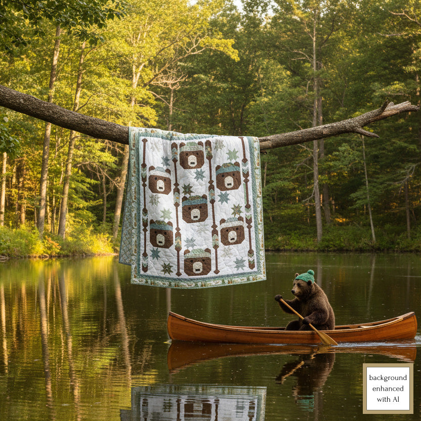 Quilt with bear pattern hanging on a tree branch over a lake with a bear in a canoe.
